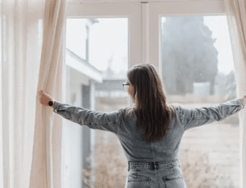 Woman from backside in denim outfit opening beige curtains